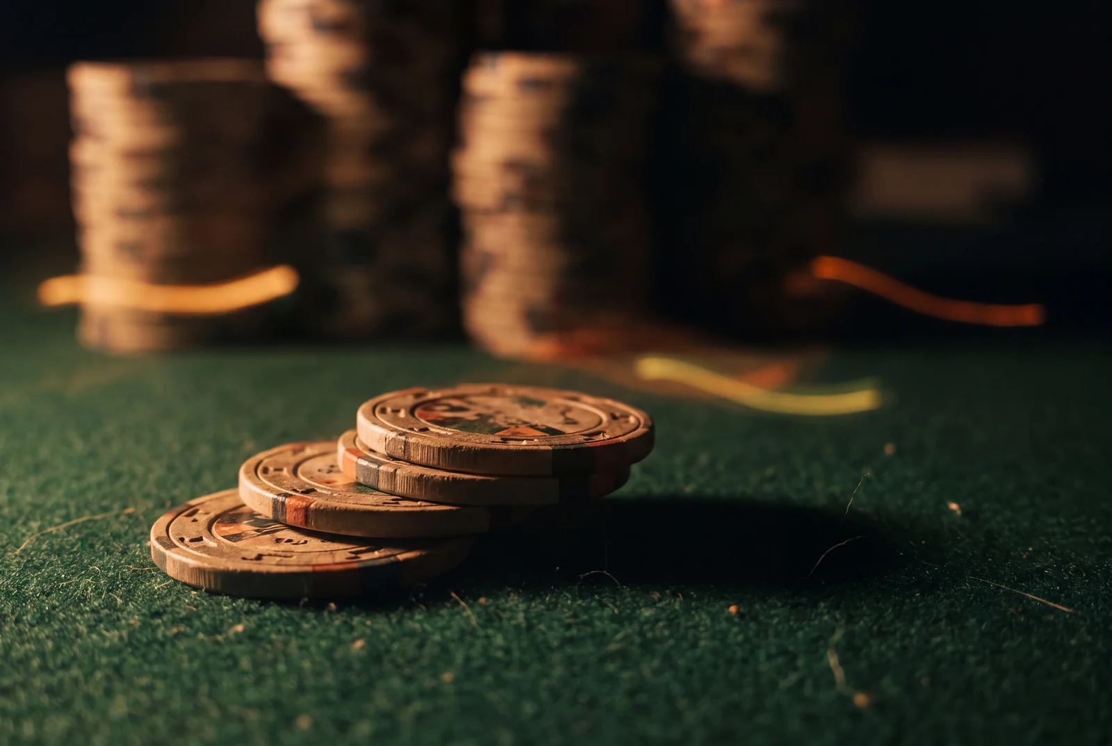 A short stack of three casino chips on green felt dwarfed by taller stacks behind